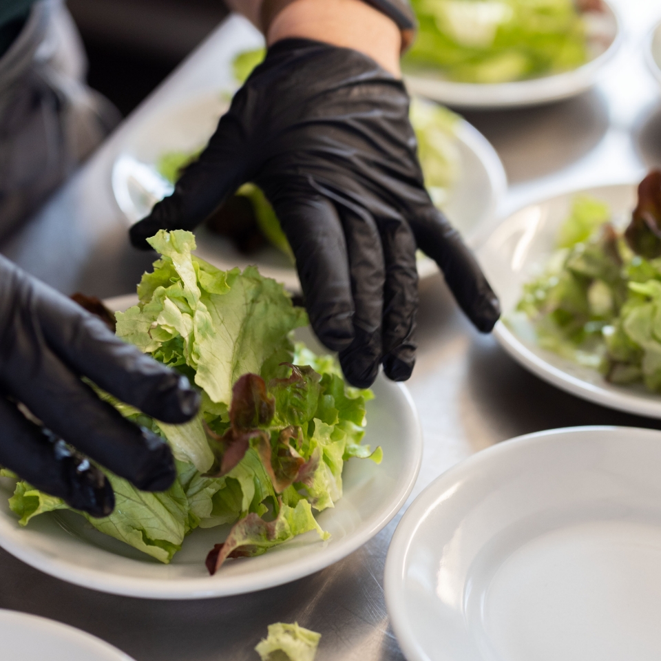 Eine PErson mit schwarzen Handschuhen richtet Salat an